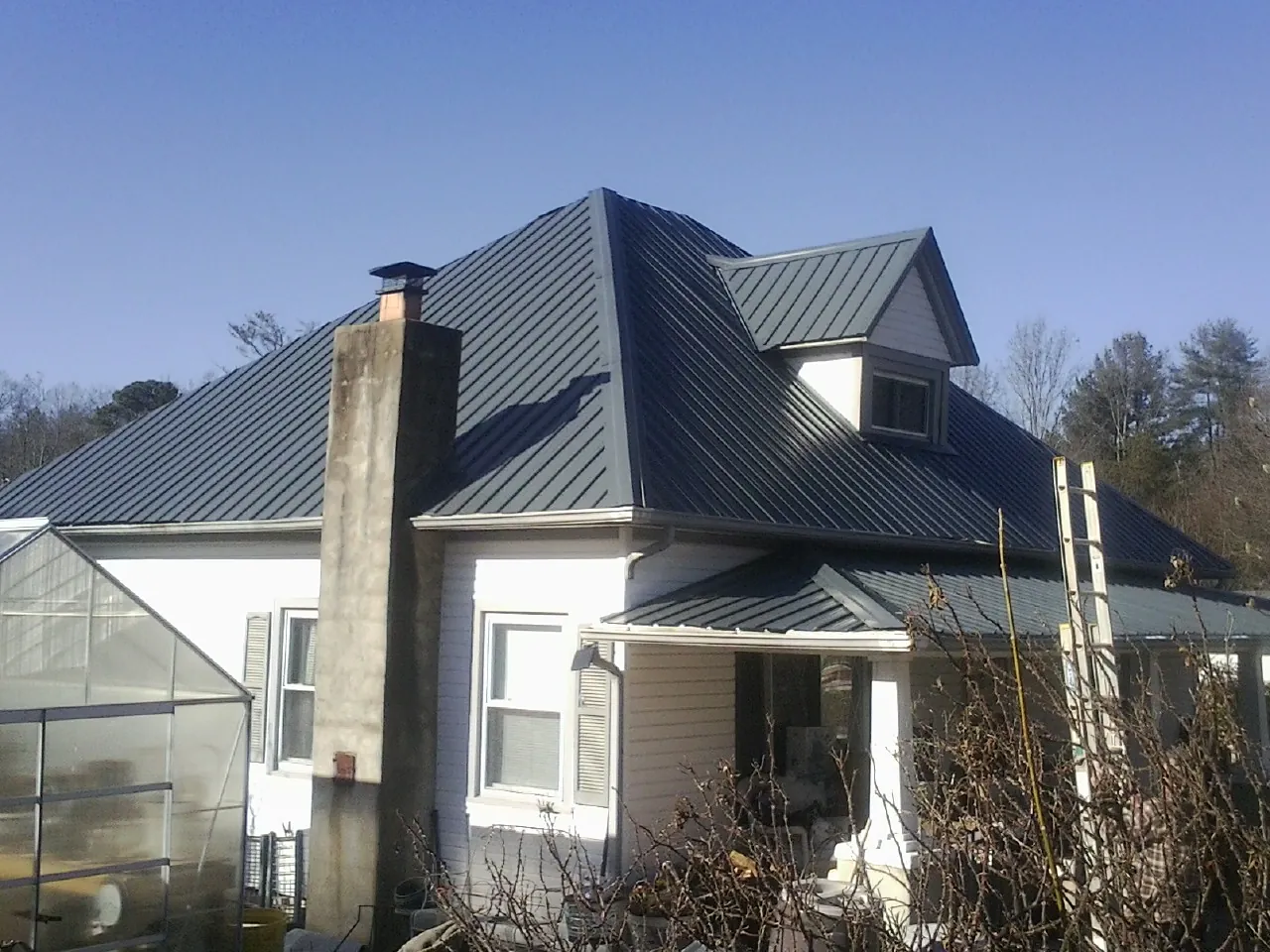 Dark blue standing seam metal roof on a white farmhouse with dormer — Slate & Tile Roof Repair by Roofing Brothers in Manchester Center