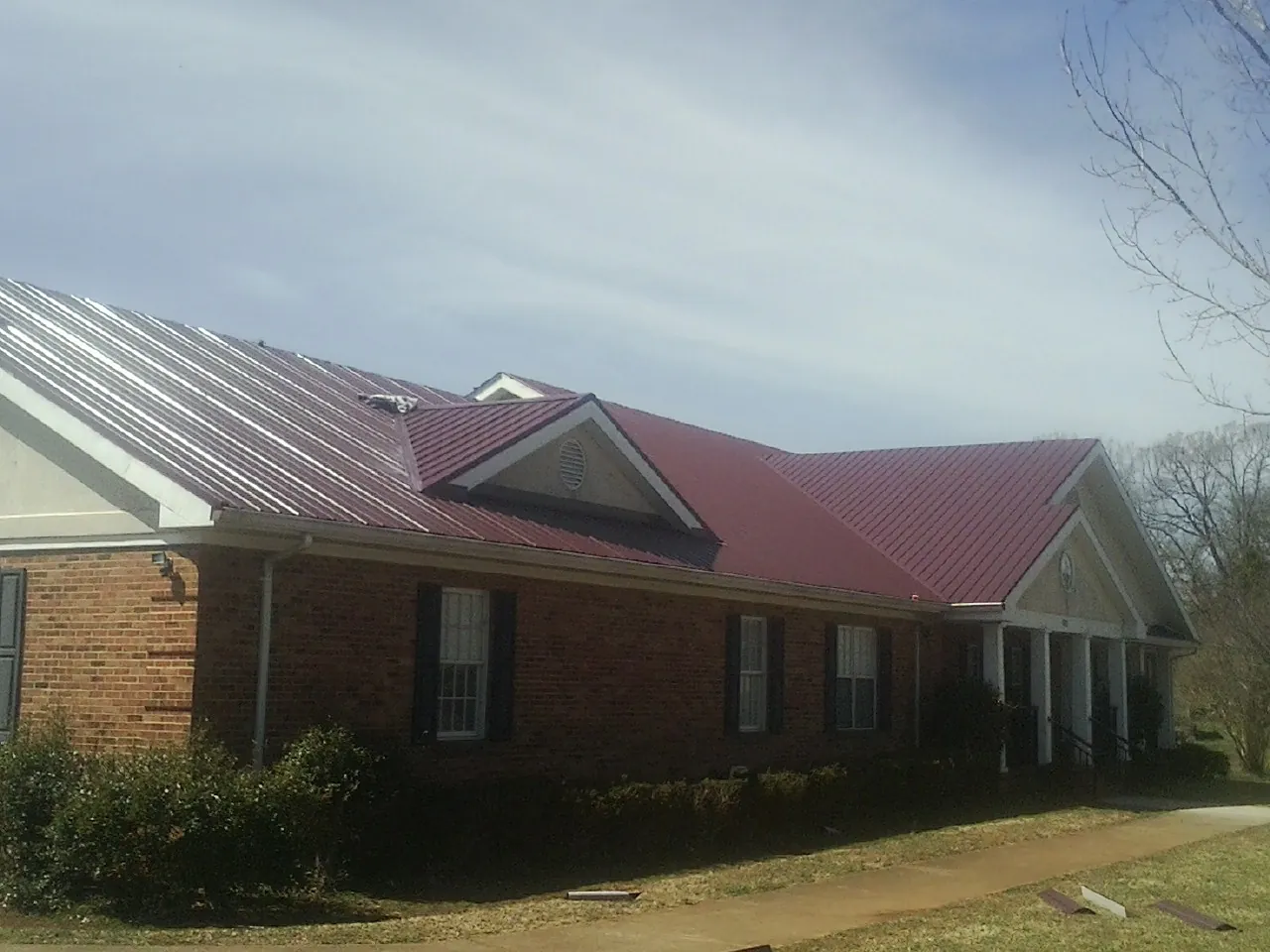 Red metal roof with gabled entries on a long brick building, from a Hail Damage Roof Repair job in Manchester Center