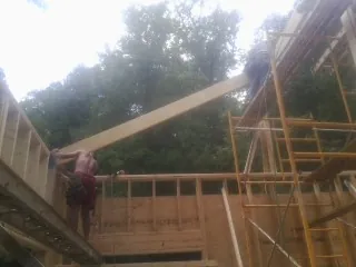 Carpenter raising a rafter beam on a new second story frame in Manchester Center