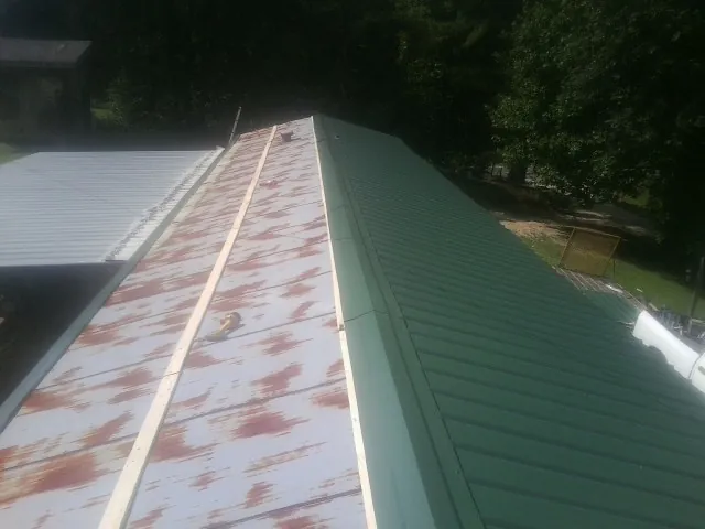 Old rusted panels beside newly installed green metal roofing — Wind Damage Roof Repair by Roofing Brothers in Manchester Center
