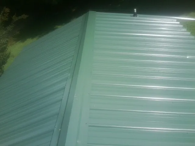 New green metal panels meeting at the ridge of a roof — Flat Roof Repair work by our crew in Manchester Center