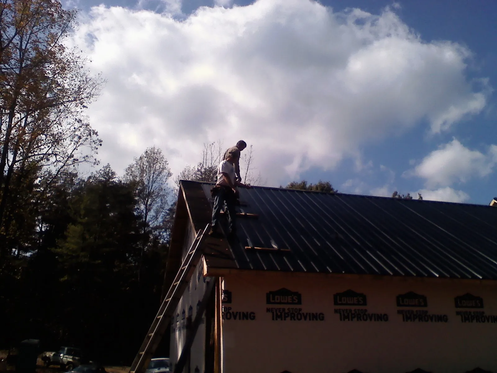 Roofer fastening dark metal panels high against a cloudy sky, from a Roof Inspection job in Manchester Center