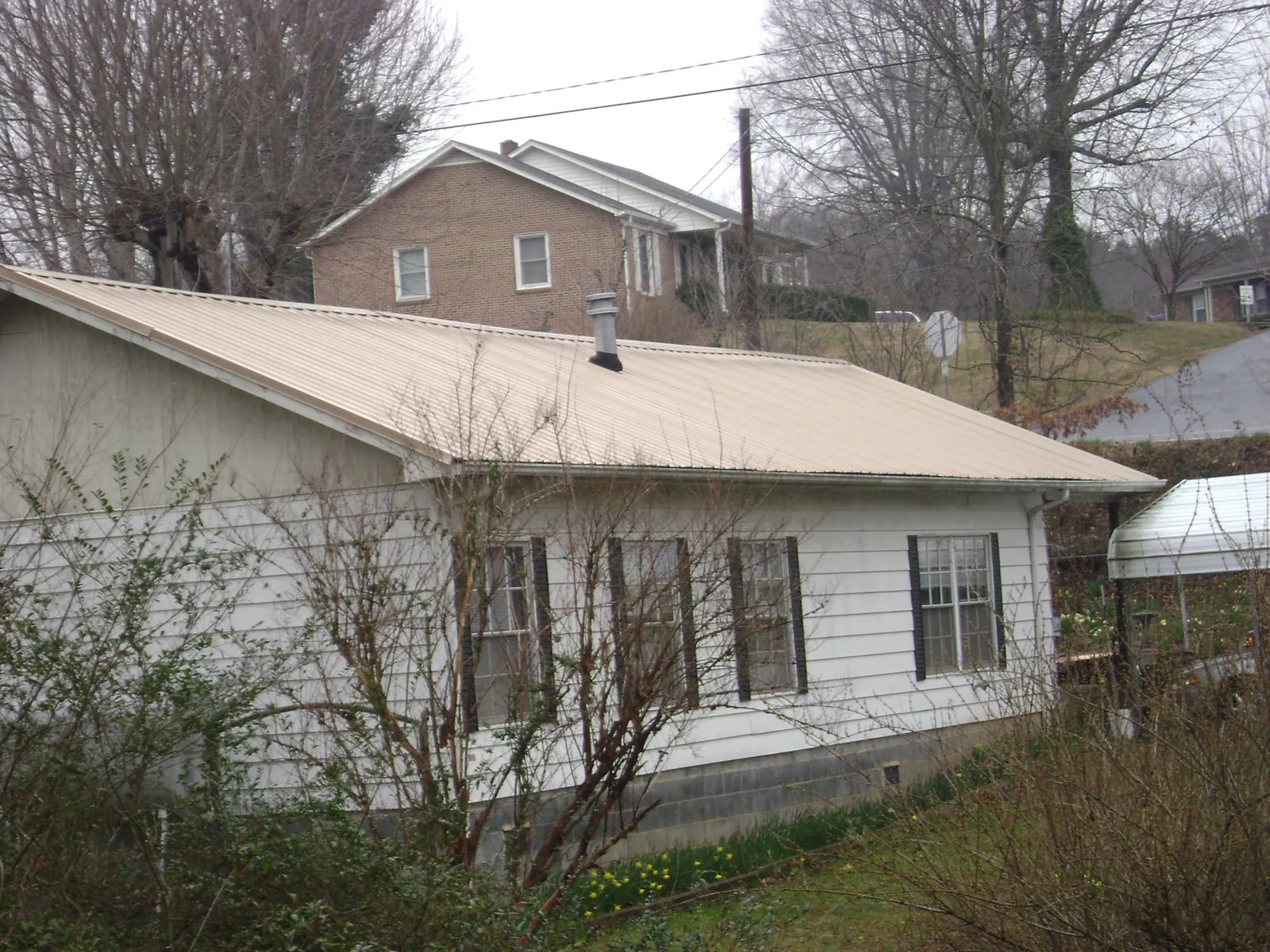 Tan metal roof on a white sided house set into a hillside — Commercial Roofing by Roofing Brothers in Manchester Center
