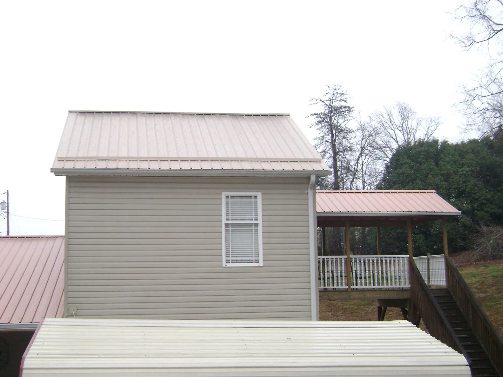 Tan metal roofs on a two story addition and attached porch, from a Roof Replacement job in Manchester Center